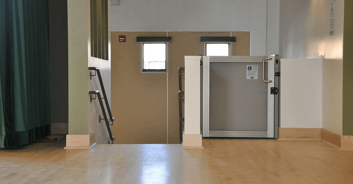 Vertical platform lift (VPL) installed in a commercial or community center entrance area with a short set of stairs, illustrating a cost-effective accessibility upgrade for a business qualifying for Section 179.
