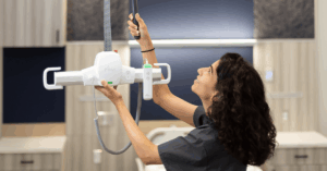 A caregiver or nurse adjusting the motorized hoist unit of a ceiling track lift system in a clean, modern medical or assisted living facility room, highlighting the system’s smooth operation for safe patient transfers.