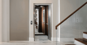 Interior view of a modern North Texas residence hallway showing an open home elevator door with a wood-paneled cab, adjacent to a staircase with a glass railing, demonstrating the seamless integration of a residential lift.
