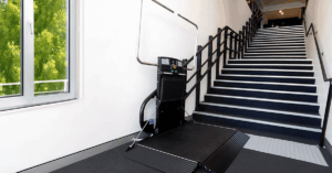Modern black Inclined Platform Lift (IPL) or Staircase Chair Lift folded at the bottom of a dark staircase in a modern commercial building, providing an accessibility solution that is an alternative to a home elevator or domestic lifts.