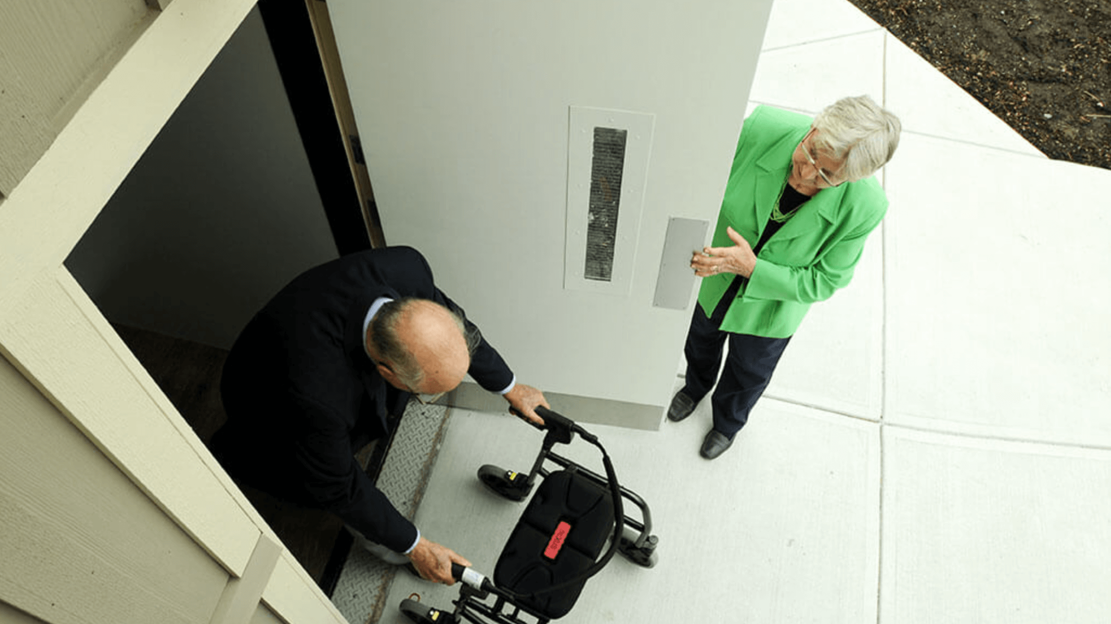A black Genesis OPAL Vertical Platform Lift installed on a reinforced concrete pad with a 42-inch top-landing safety gate—a compact, TAS-compliant accessibility solution for DFW commercial projects.