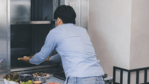 A person loading a tray of food into a stainless steel home dumbwaiter lift.