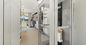 Modern home elevator with a clear glass door integrated seamlessly into a spacious white luxury walk-in closet.