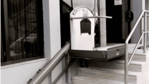An adult child helping an aging parent use a vertical platform lift at the front entry steps of a North Texas home